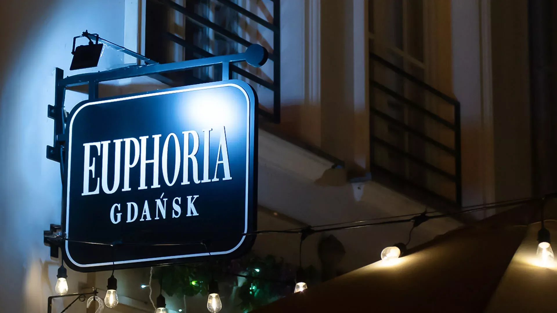 Euphoria Gdansk - loodrechte semafoor, dubbelzijdig in zwart met witte letters bij nacht